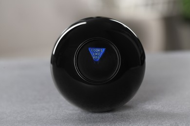 Photo of Magic eight ball with prediction Looks Like Yes on light gray table, closeup