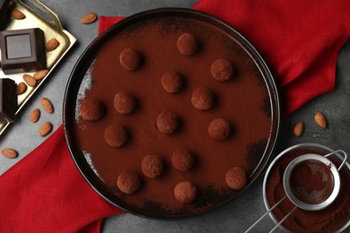 Photo of Delicious chocolate candies powdered with cocoa, sieve and ingredients on grey table, flat lay
