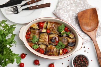 Tasty eggplant rolls with tomatoes, cheese and parsley in baking dish on white wooden table, flat lay