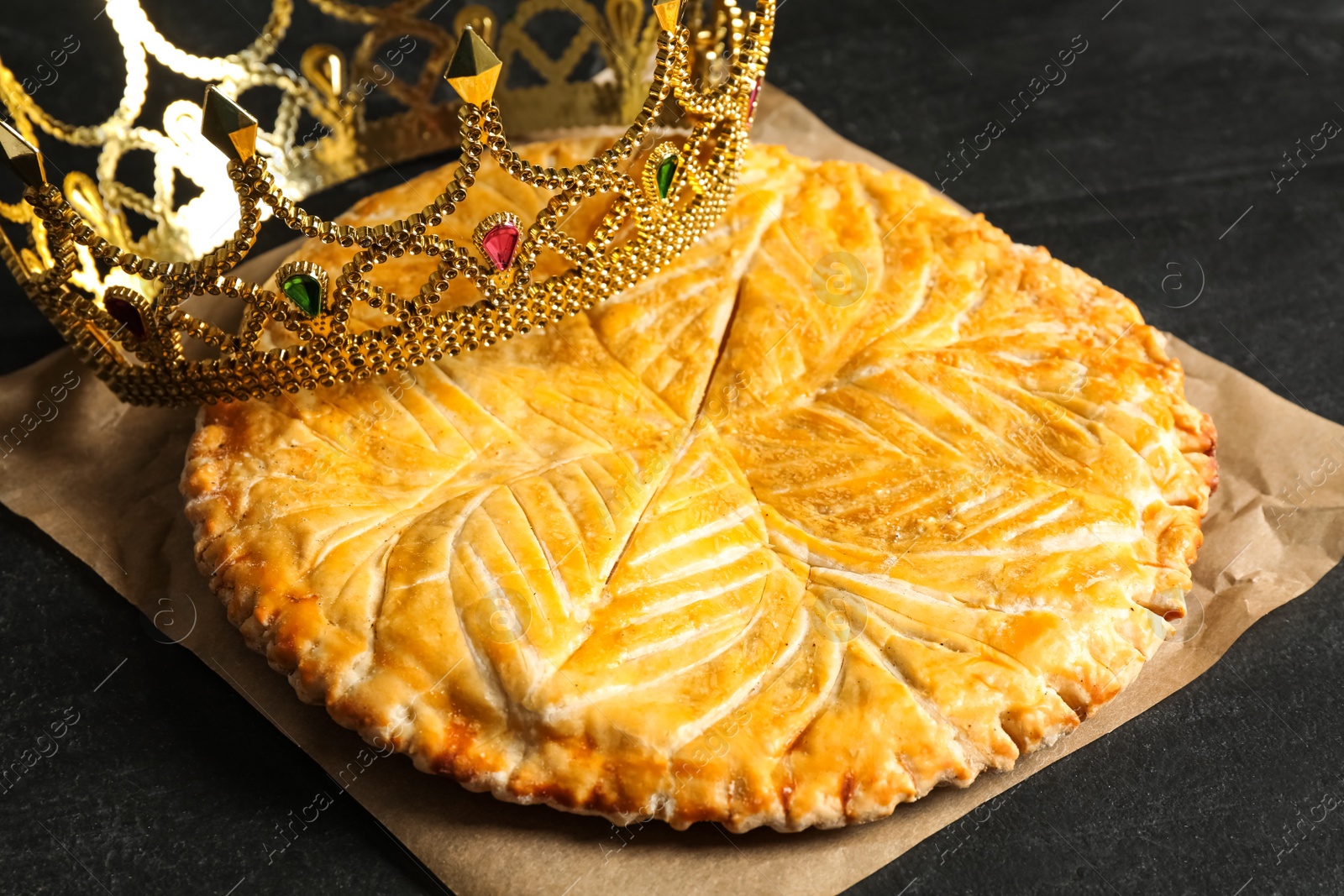 Photo of Traditional galette des Rois with decorative crown on black table, closeup