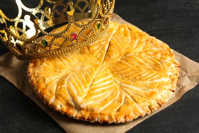 Photo of Traditional galette des Rois with decorative crown on black table, closeup