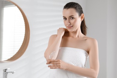 Photo of Beautiful woman applying body cream onto elbow in bathroom, space for text