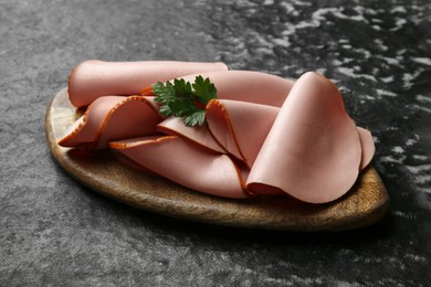 Photo of Board with slices of tasty boiled sausage and parsley on dark textured table