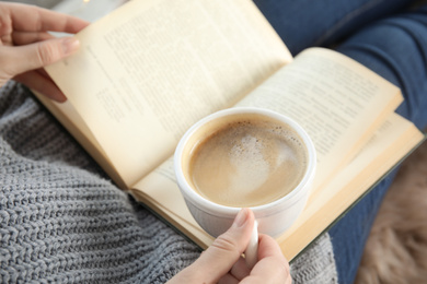 Woman with cup of coffee reading book at home, closeup