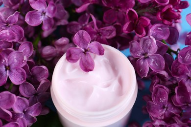 Photo of Jar of cream and lilac beautiful flowers as background, closeup