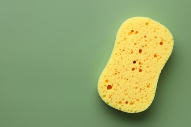 New yellow sponge on green background, top view. Space for text