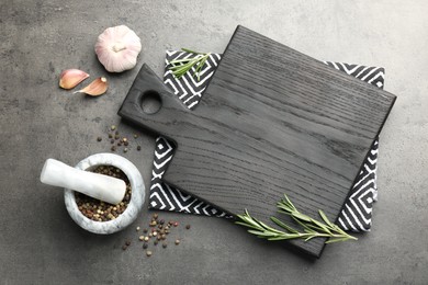 Black cutting board, napkin and spices on grey table, flat lay