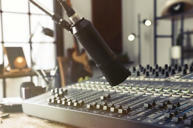 Photo of Microphone near table with professional mixing console in radio studio, closeup