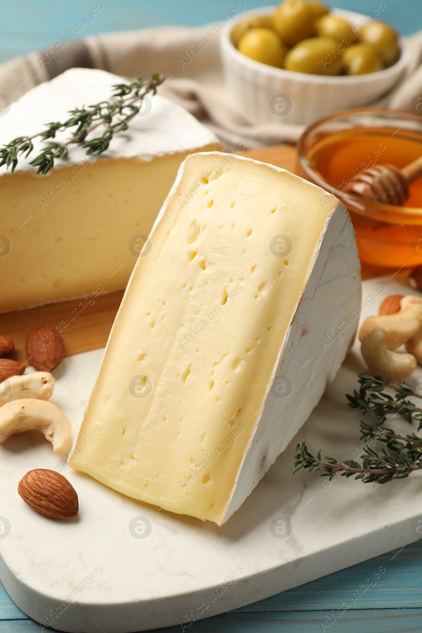 Photo of Tasty Camembert cheese with thyme, honey and nuts on light blue wooden table