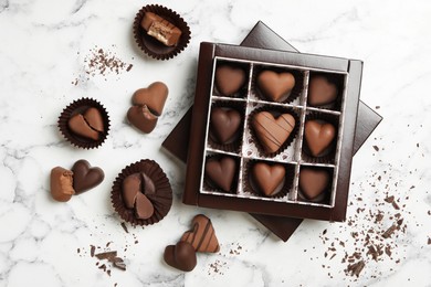 Delicious heart shaped chocolate candies on white marble table, flat lay