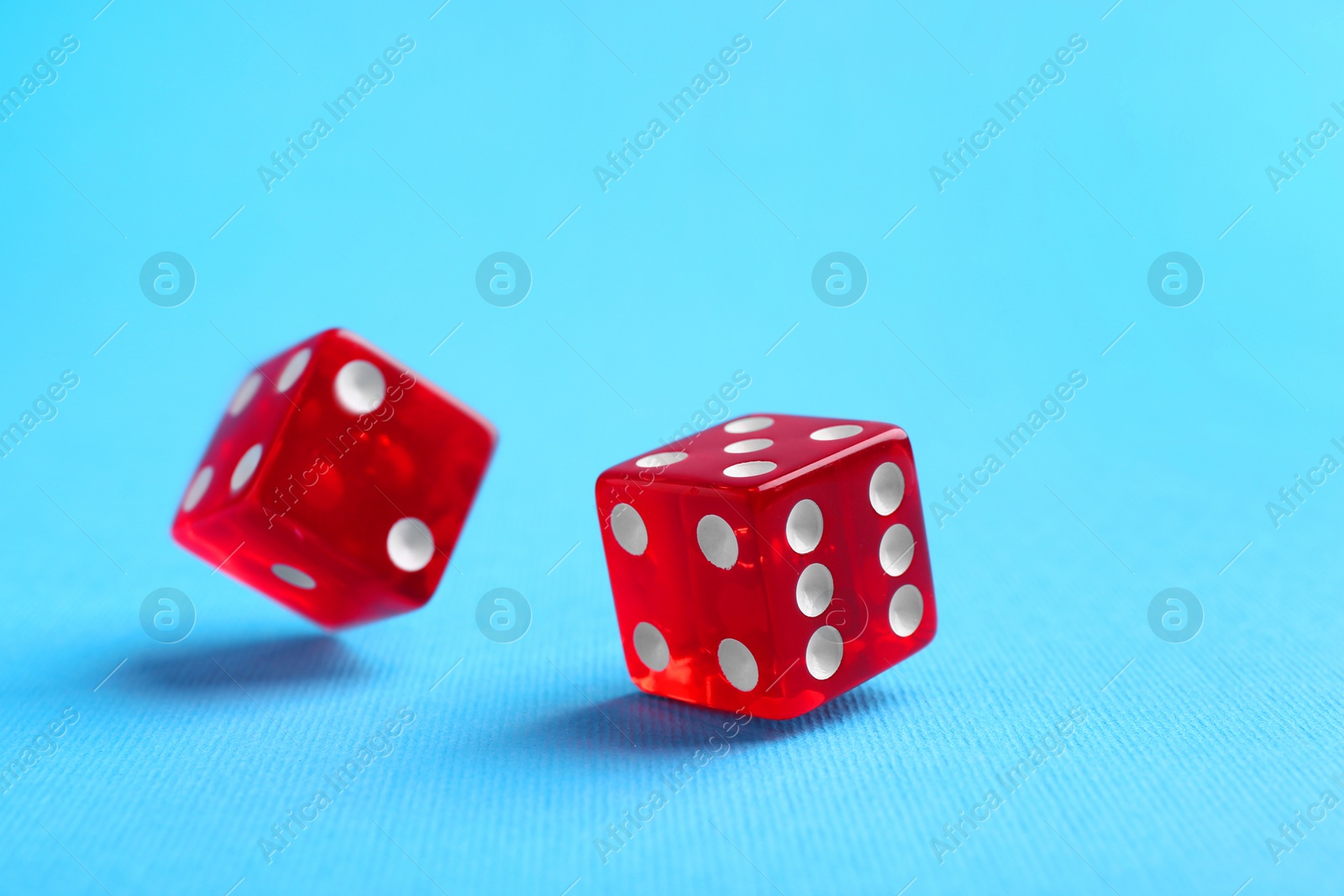 Photo of Two red game dices falling on light blue background, closeup