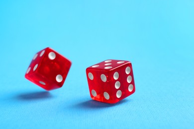 Photo of Two red game dices falling on light blue background, closeup