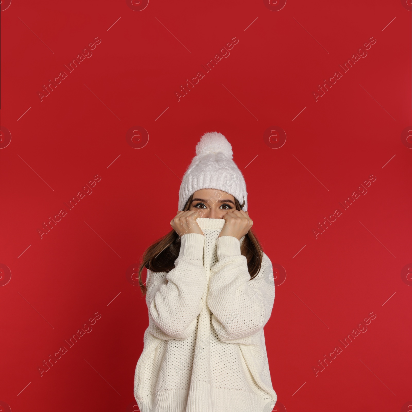 Photo of Beautiful young woman in white sweater and hat on red background. Winter season