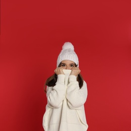 Beautiful young woman in white sweater and hat on red background. Winter season