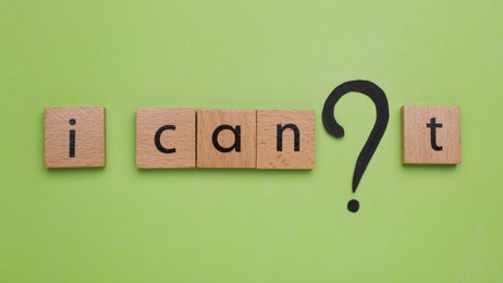 Photo of Motivation concept. Changing phrase from I Can't into I Can by removing wooden cube with letter T on light green background, flat lay