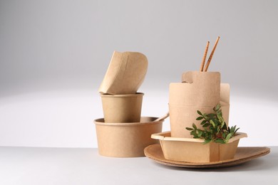 Photo of Eco friendly food packaging. Paper containers, tableware and green twigs on light background, space for text