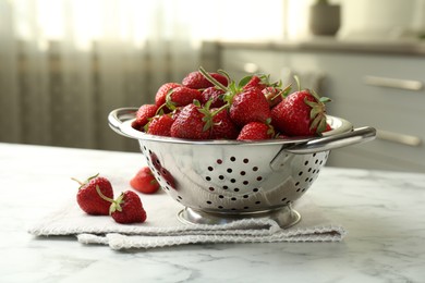 Photo of Metal colander with fresh strawberries on white marble table in kitchen