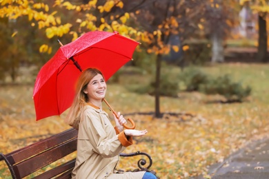 Woman with umbrella sitting on bench in autumn park. Rainy day