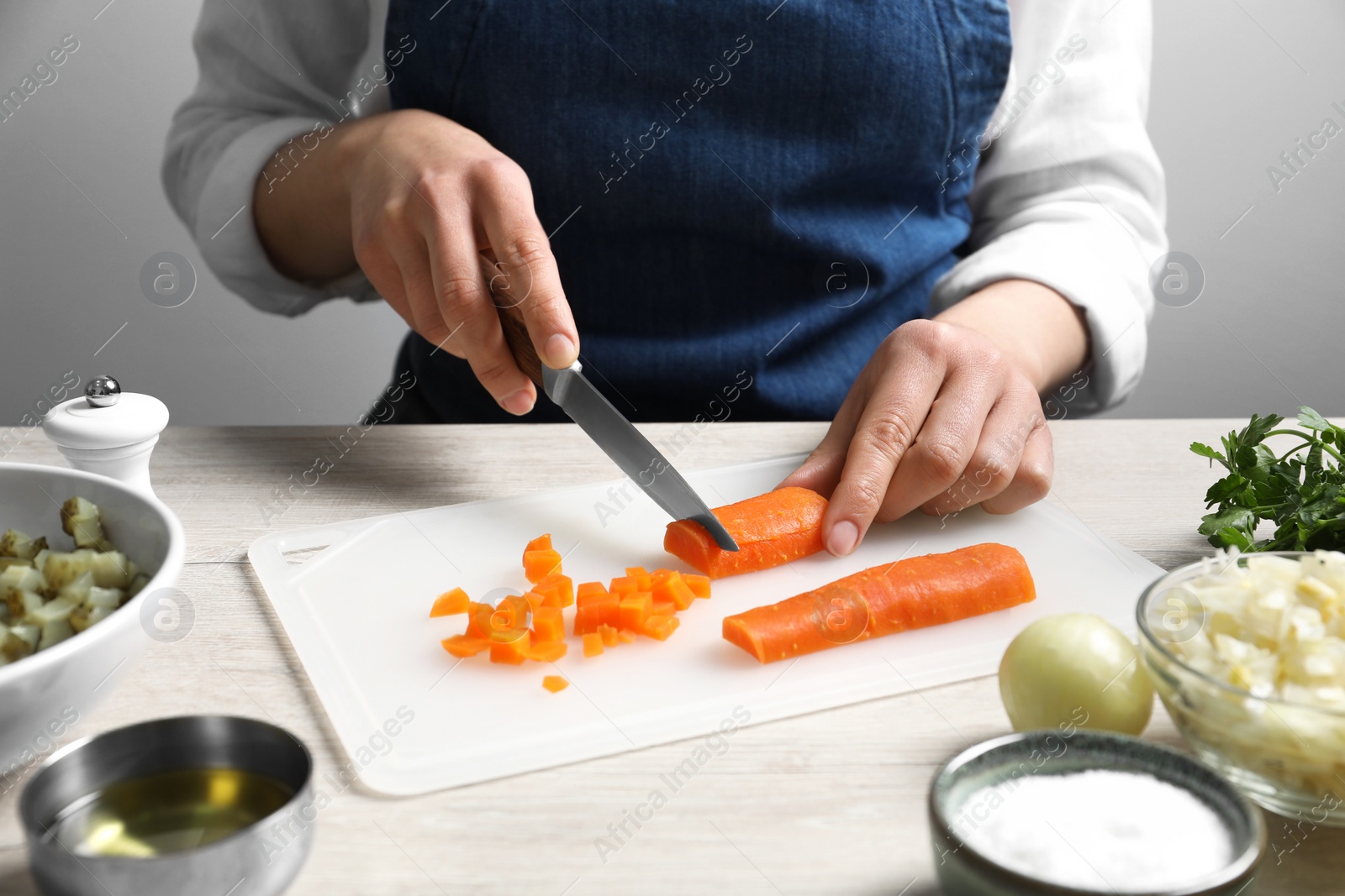 Photo of Woman cutting boiled carrot at white wooden table, closeup. Cooking vinaigrette salad