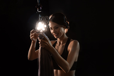 Photo of Young woman preparing aerial silk for acrobatic performance on dark background