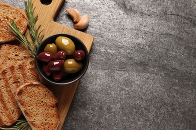 Tasty bruschettas, olives, rosemary and garlic on grey table, flat lay. Space for text