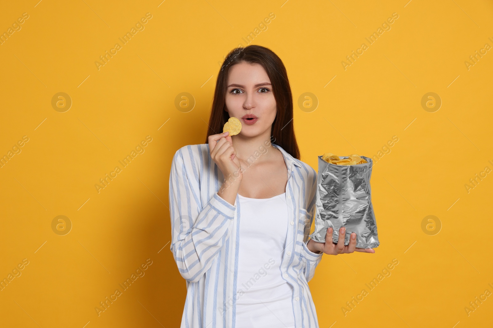 Photo of Pretty young woman with bag of tasty potato chips on yellow background