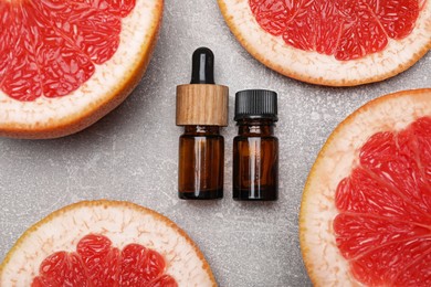 Photo of Bottles of essential oil with grapefruit slices on grey table, flat lay