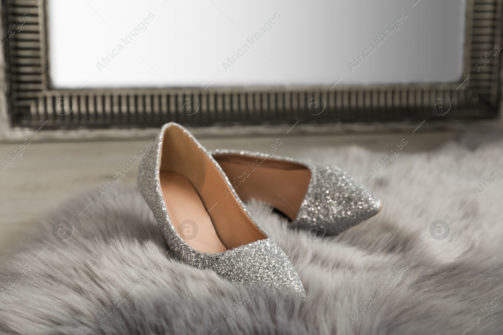 Photo of Stylish shiny high heeled shoes on faux fur near mirror in room
