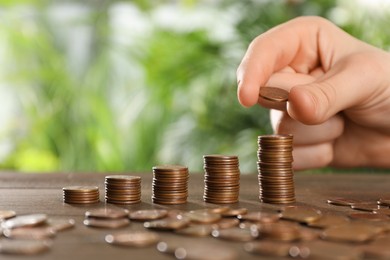 Photo of Woman stacking coins at wooden table against blurred green background, closeup. Space for text