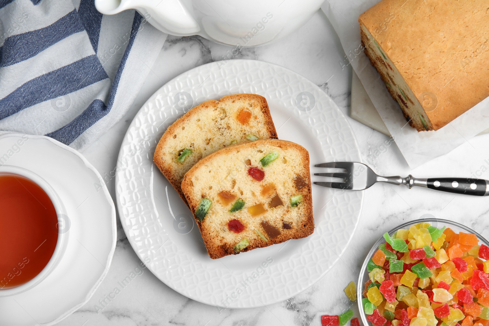 Photo of Delicious cake with candied fruits and tea on white marble table, flat lay