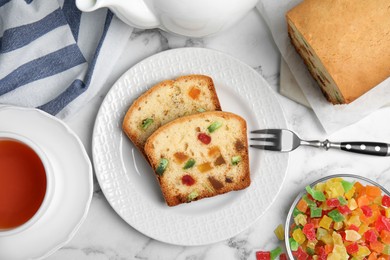 Delicious cake with candied fruits and tea on white marble table, flat lay