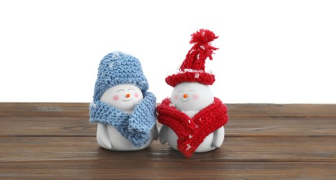 Cute decorative snowmen in hats and scarves on wooden table against white background