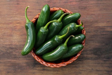 Photo of Bowl with green jalapeno peppers on wooden table, top view