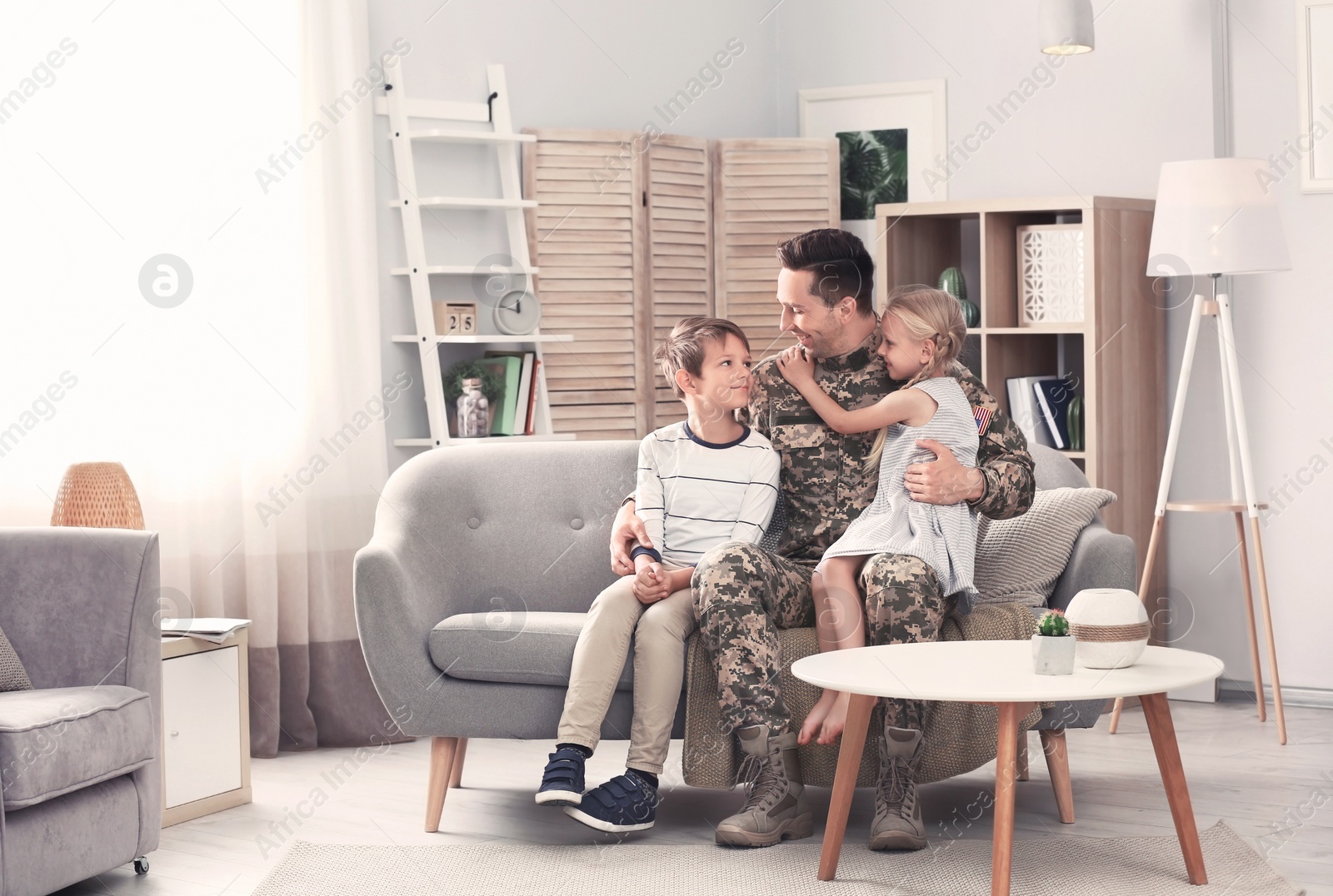 Photo of Young man in military uniform with his children on sofa at home