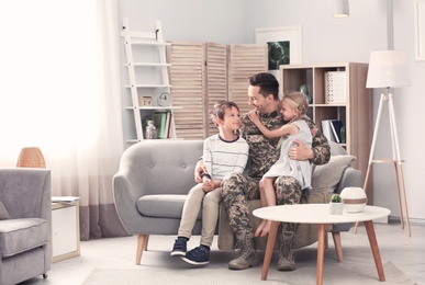 Young man in military uniform with his children on sofa at home