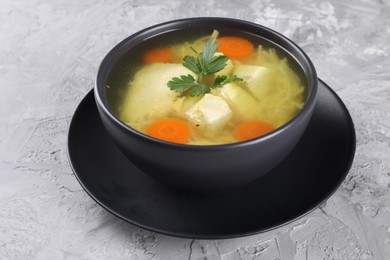 Tasty chicken soup with noodles, carrot and parsley in bowl on light textured table, closeup