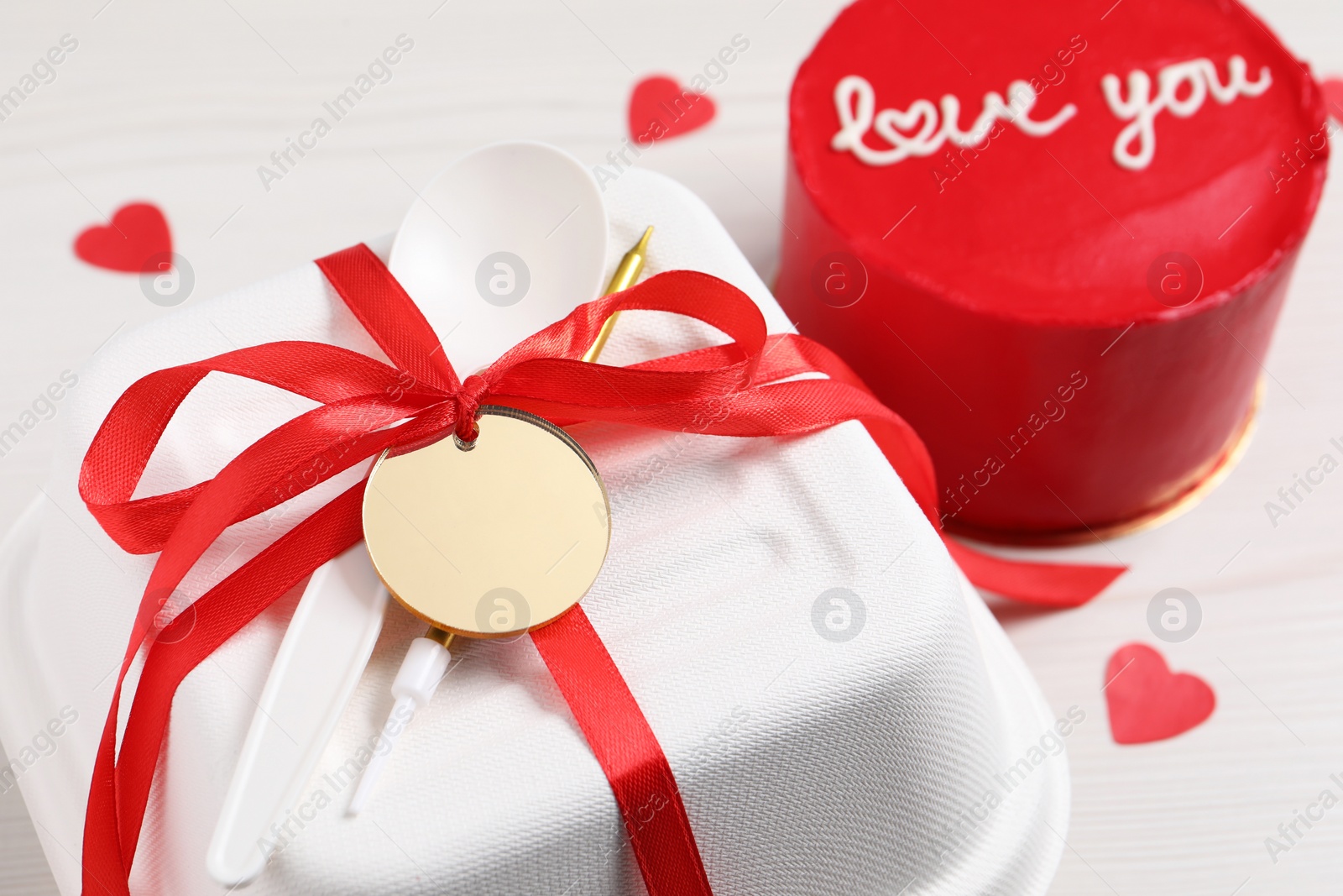 Photo of Bento cake with text Love You, takeaway packaging and paper hearts on white wooden table, closeup. St. Valentine's day surprise