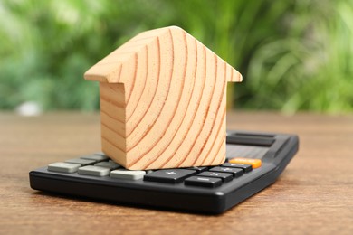 Photo of Mortgage concept. House model and calculator on wooden table against blurred green background, closeup