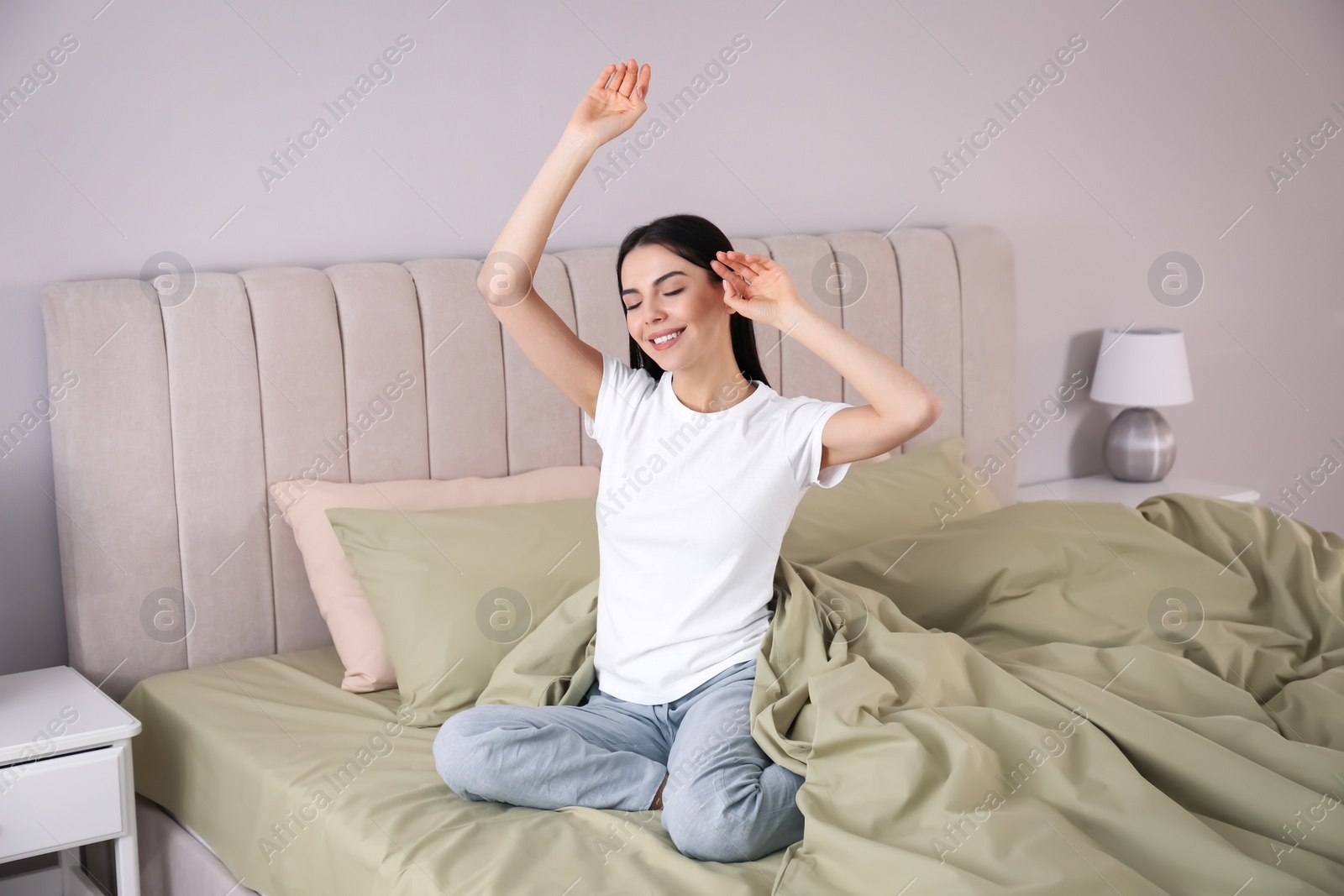 Photo of Woman stretching on comfortable bed with green linens