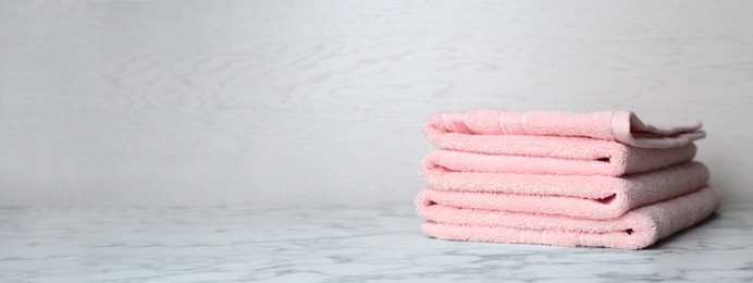 Image of Stack of folded pink towels on white marble table against light background, space for text. Banner design
