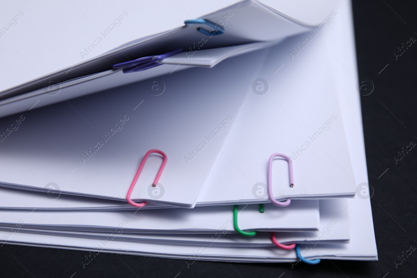 Photo of Sheets of paper with clips on black background, closeup