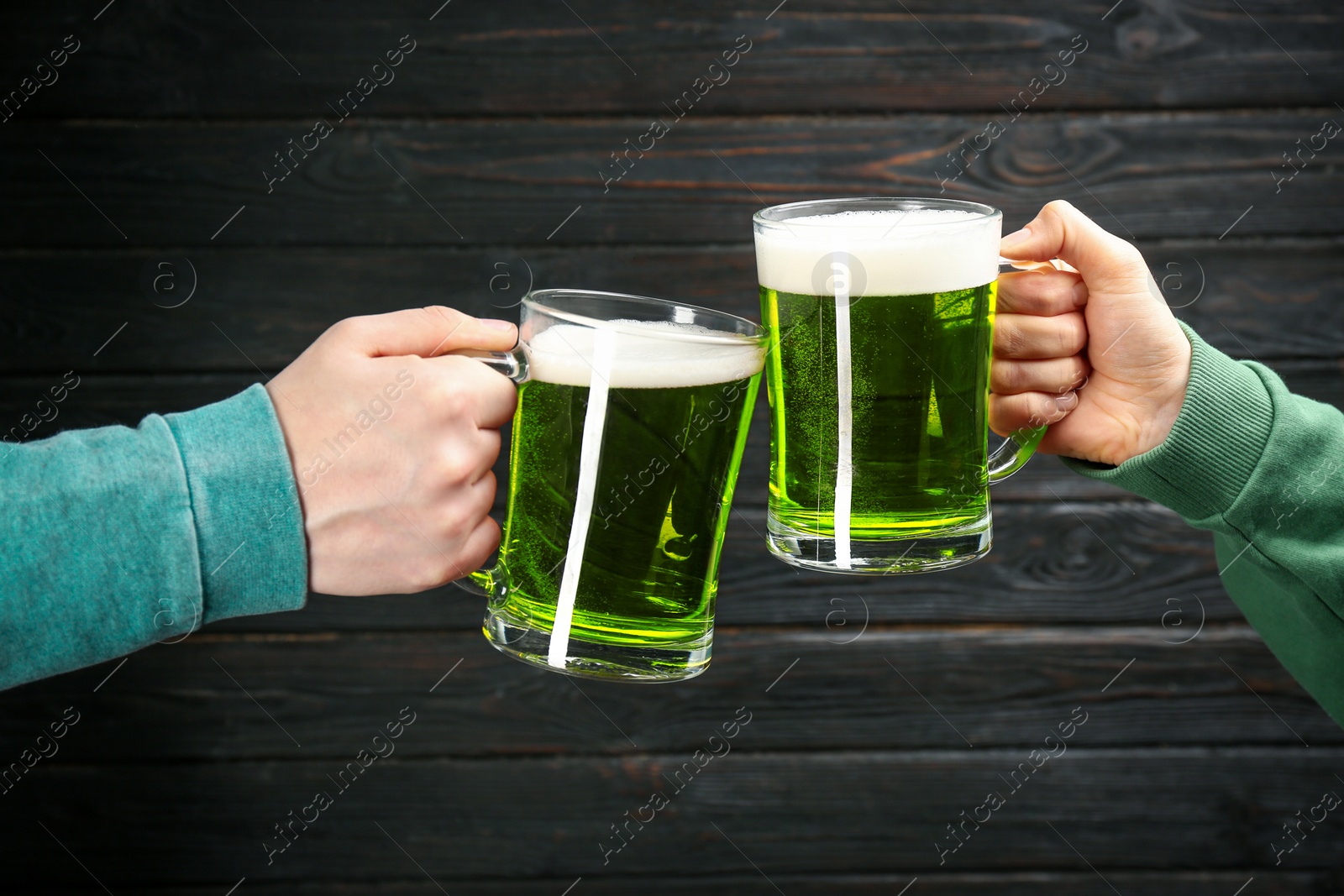 Photo of Man and woman toasting with green beer on black wooden background, closeup. St. Patrick's Day celebration