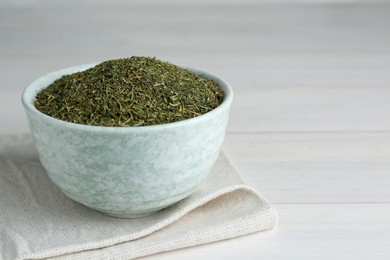 Photo of Dried dill in bowl on white wooden table, closeup. Space for text