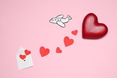 Photo of Long-distance relationship concept. Decorative hearts flying out of envelope and paper airplane on pink background, flat lay