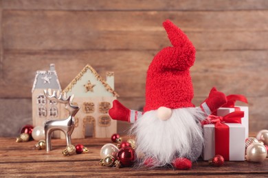 Photo of Cute Christmas gnome, gift boxes and festive decor on table against wooden background