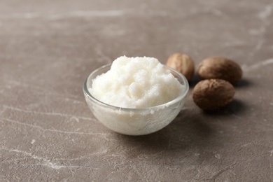 Photo of Shea butter in bowl and nuts on grey background