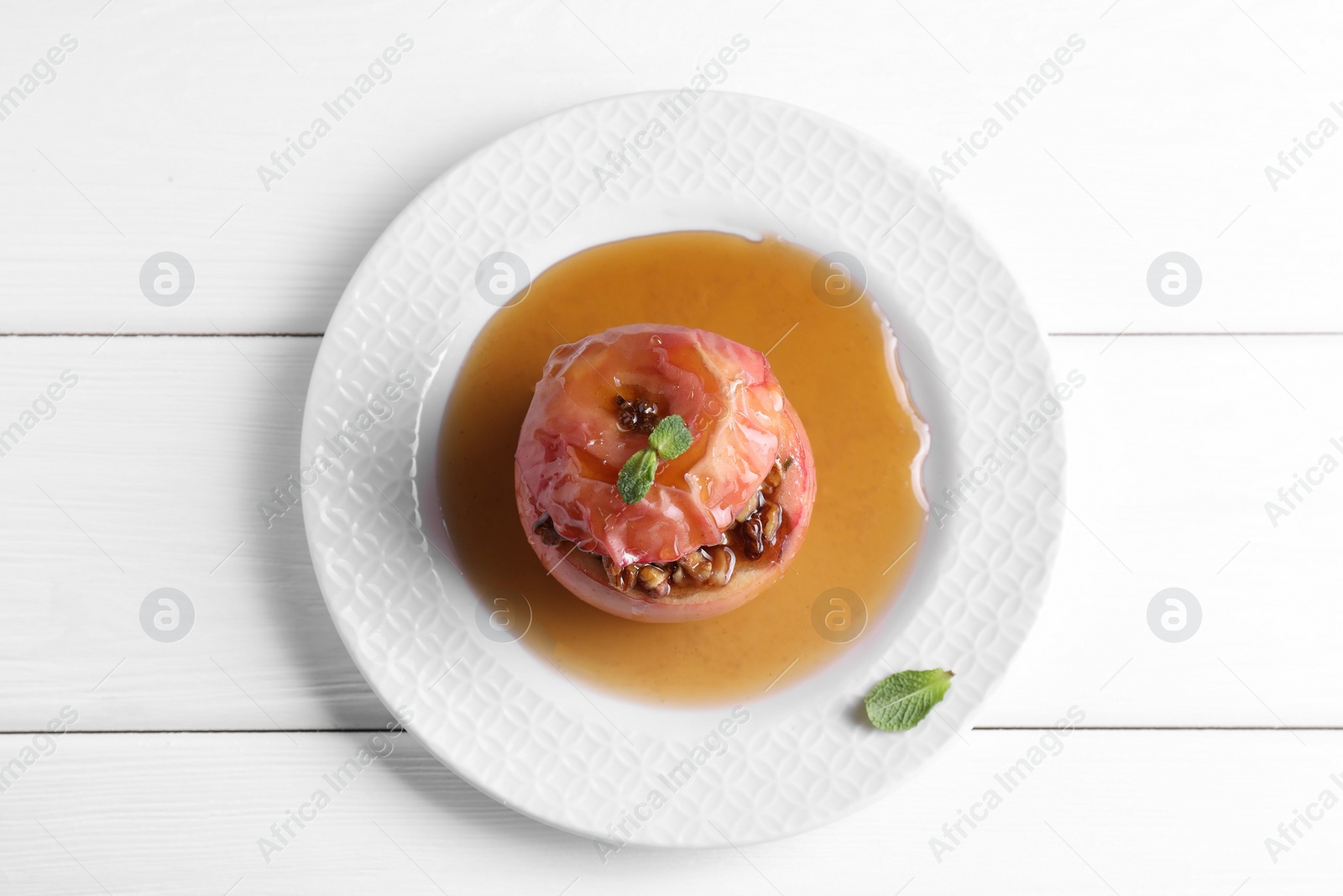 Photo of Tasty baked apple with nuts, honey and mint on white wooden table, top view