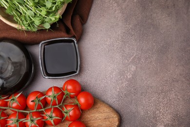 Organic balsamic vinegar, tomatoes and greens on grey table, flat lay. Space for text