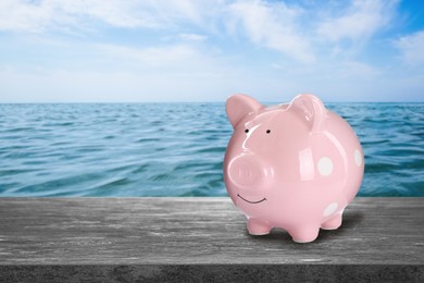 Image of Saving money for summer vacation. Piggy bank on stone surface near sea, space for text