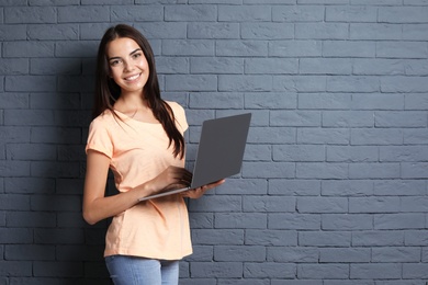 Photo of Young woman with modern laptop on brick wall background